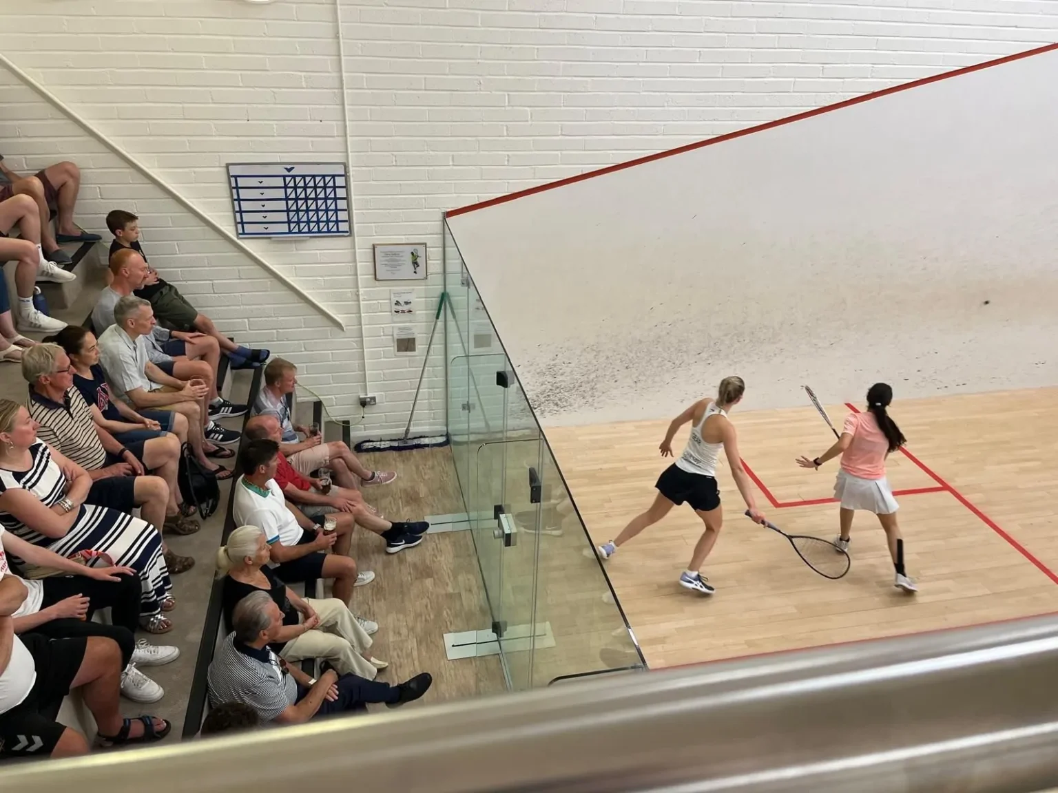 Two women playing squash on an indoor court with audience.